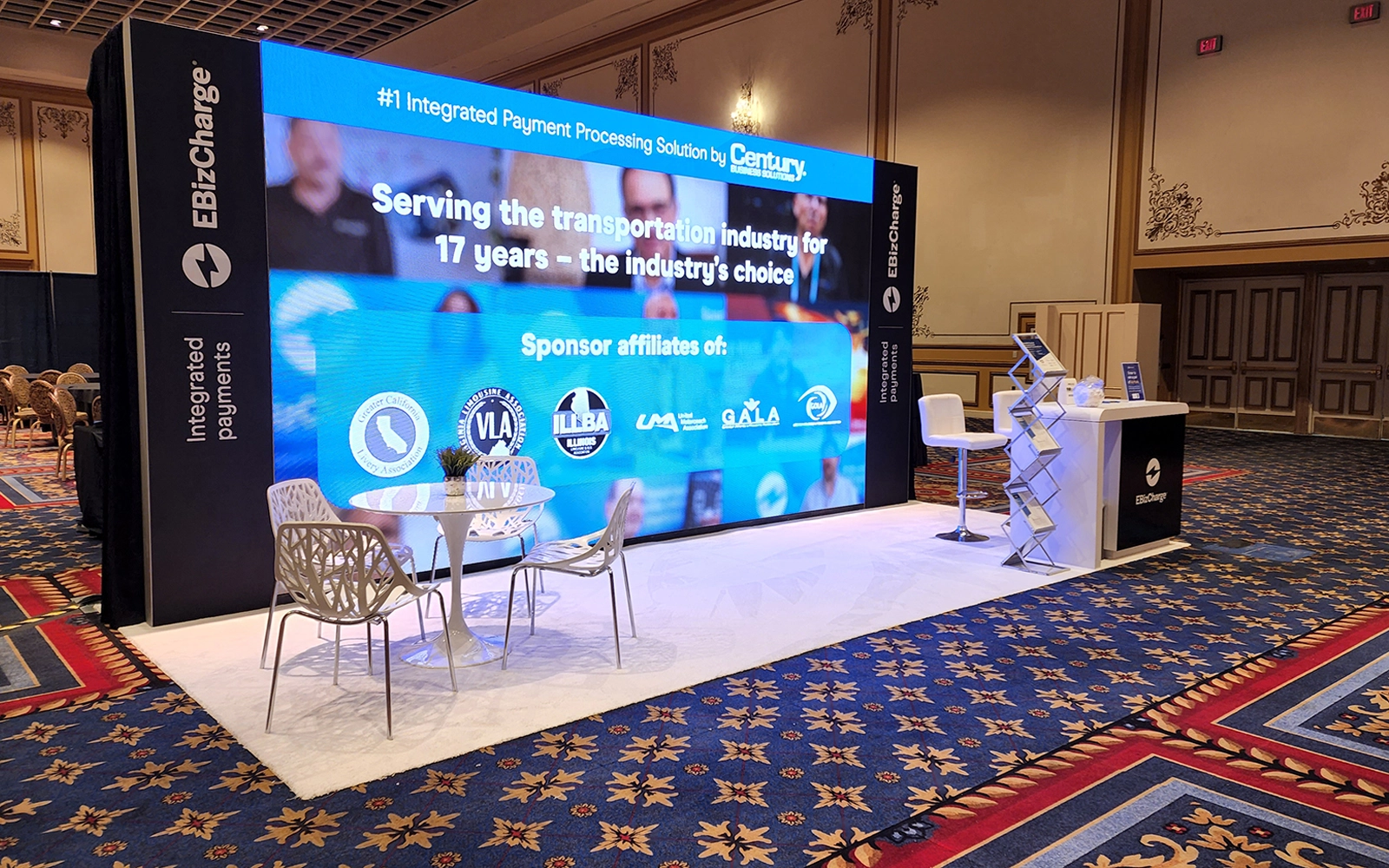 20x10 trade show booth designs with LED video wall lounge, reception counter, branded side towers, meeting table and open booth space
